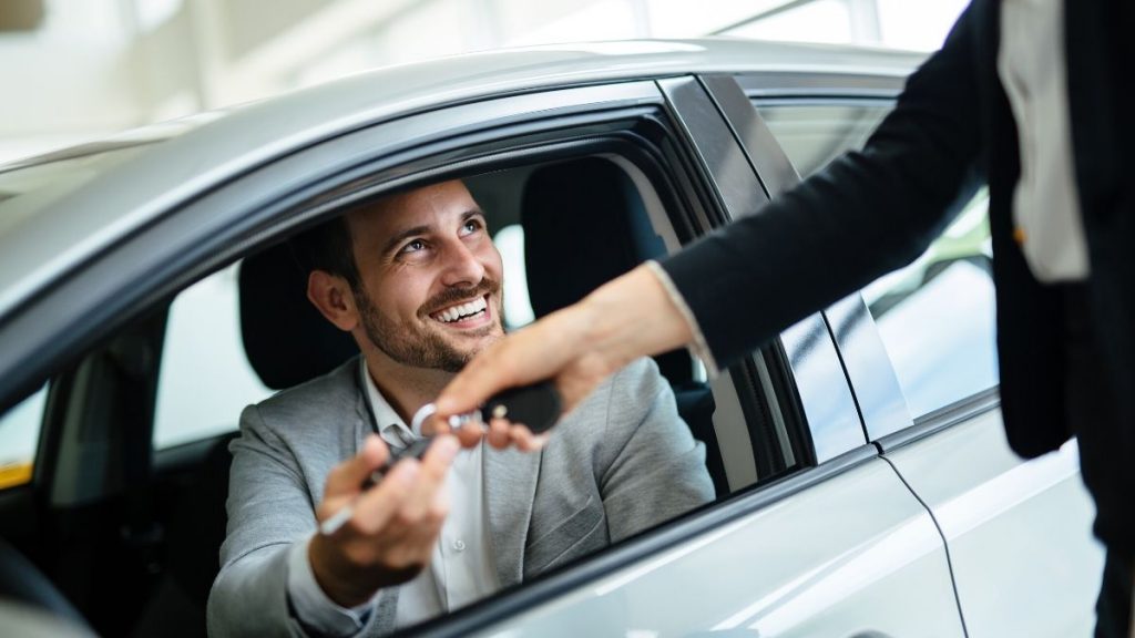 Guy in suit handing over keys to guy in car